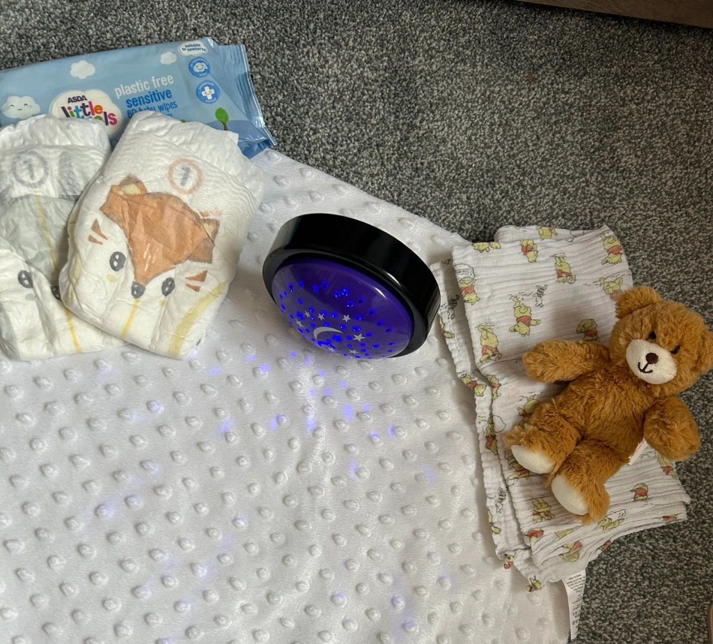 A blanket, 2 nappies, a pack of baby wipes, a light, a muslin cloth and toy